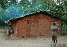 Old Pygmy woman in front of a mud hut